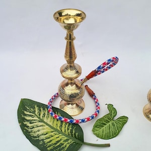 Może przedstawiać: Złoty kolor fajki wodnej ze skomplikowanymi rzeźbieniami i wzorzystym wężem w kolorze czerwonym, białym i niebieskim. Fajka wodna ma misę, trzon i podstawę. Wąż jest połączony z podstawą za pomocą skórzanego łącznika. Fajka wodna to przedmiot dekoracyjny.