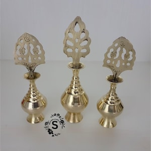 May include: Three gold metal perfume bottles with ornate, decorative tops. The bottles are all different shapes and sizes. The tops are all different designs, but they all have a similar style. The bottles are all sitting on a white surface.
