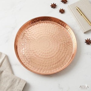 May include: A round copper tray with a hammered texture. The tray has a raised edge and a polished finish. The tray is surrounded by star anise, a notebook, and a pen. The tray is approximately 12 inches in diameter.