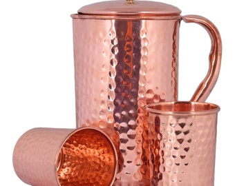 May include: A set of three hammered copper drinking glasses and a pitcher with a lid. The glasses and pitcher have a shiny, metallic finish.
