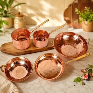 May include: A set of copper kitchen cookware with hammered textures. The set includes two saucepans with long handles, two pans with handles, and a wok-style bowl. The copper color is warm and inviting.