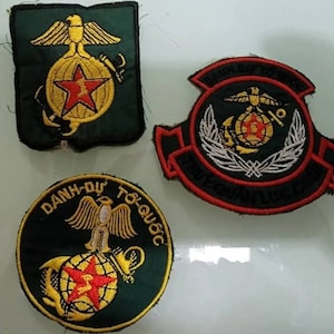 May include: Three embroidered patches with a green background and yellow, red, and white thread. The patches feature a globe with a star, an eagle, and the text "DANH-QUY TO QUOC".