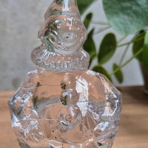 Puede incluir: Una figurita de vidrio transparente de un payaso con un sombrero puntiagudo. El payaso sostiene una pelota en su mano.