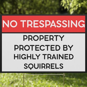 May include: A rectangular sign with the words "NO TRESPASSING" in red and white. Below, it reads "PROPERTY PROTECTED BY HIGHLY TRAINED SQUIRRELS" in black text. The sign is on a metal stake in a grassy area.