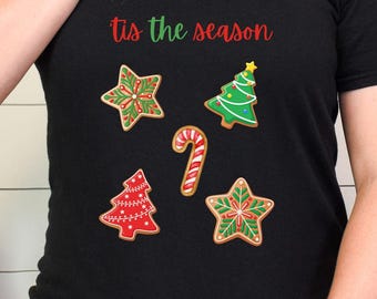 May include: Black t-shirt with the phrase "tis the season" in red script. The shirt features gingerbread cookie designs: stars, Christmas trees, and a candy cane, all in festive colors.