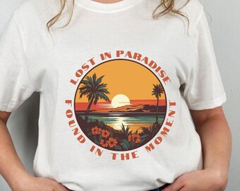 May include: White t-shirt with a retro-style graphic of a sunset over a beach with palm trees and the text "Lost in Paradise Found in the Moment".
