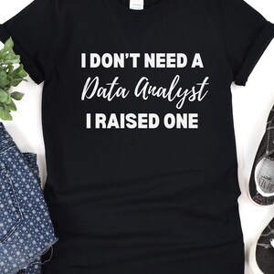 May include: Black t-shirt with white text that reads "I don't need a Data Analyst I raised one".
