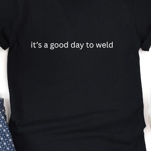 May include: Black t-shirt with the white text "it's a good day to weld". The shirt has short sleeves and a crew neck. The fabric appears to be a soft cotton blend. The shirt is a casual wear item.