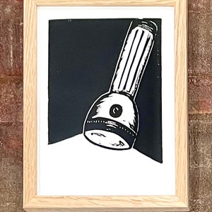 Puede incluir: Una impresión de linóleo en blanco y negro de una linterna que brilla en la oscuridad. La linterna está inclinada hacia la parte inferior de la imagen, creando un área blanca brillante.