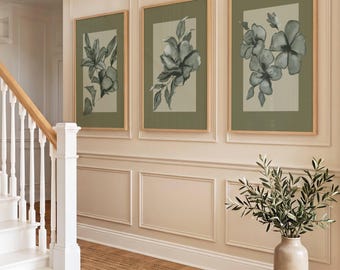May include: A set of three rectangular wall art prints featuring dark green botanical illustrations of flowers and leaves on a light beige background, each enclosed in a light wood frame and displayed in a vertical orientation on a paneled wall.