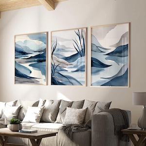 May include: Three abstract landscape paintings in blue and grey tones. The paintings are framed in natural wood and feature a stylised depiction of mountains and water.