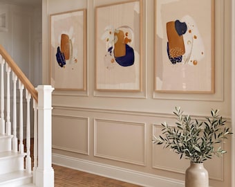 May include: Three framed vertical wall art prints featuring abstract compositions of navy blue, burnt orange, and cream shapes. Each print is encased in a light wood frame, displaying organic brushstrokes, dotted textures, and layered color blocks.