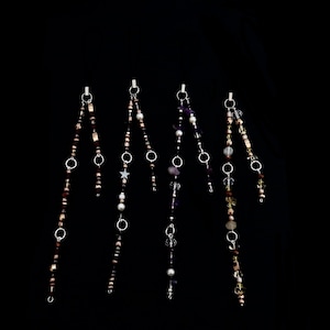 May include: Five strands of beaded jewellery with different coloured beads and charms. Each strand has a silver clip at the top and features a variety of beads, including clear, purple, brown, gold, and white.