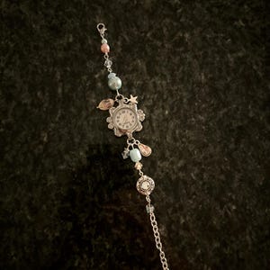 May include: A silver charm bracelet with a small watch face, blue and pink beads, and a star charm.