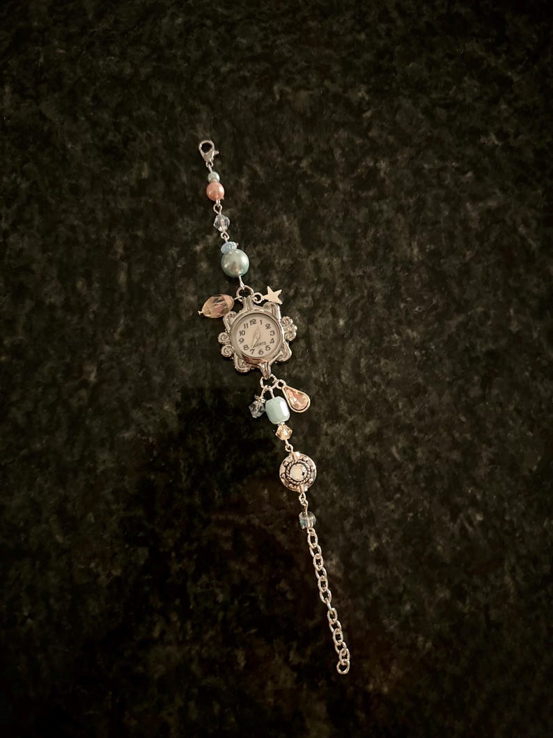 May include: A silver charm bracelet with a small watch face, blue and pink beads, and a star charm.