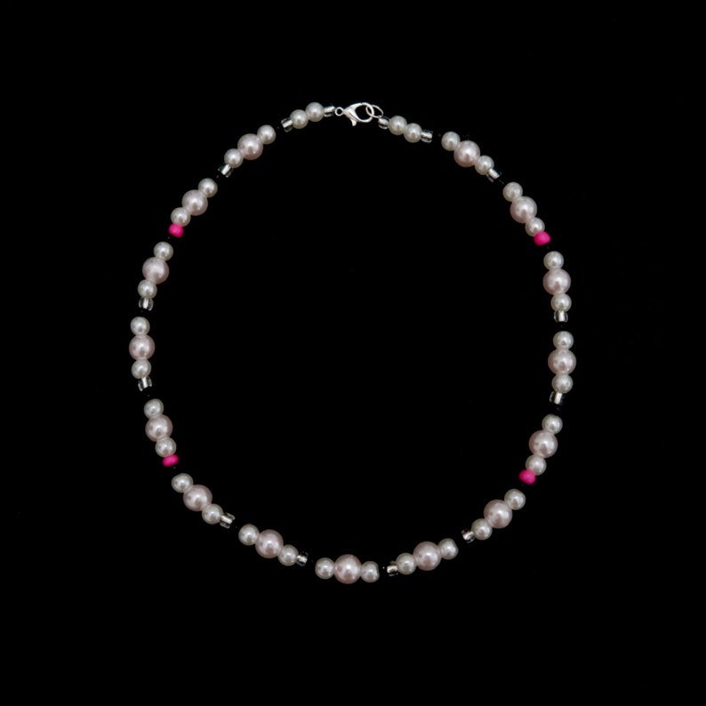 May include: A white pearl necklace with black and pink beads. The necklace has a silver clasp.