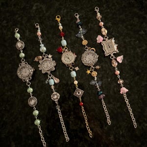 May include: Six charm bracelets with different colored beads and charms, each featuring a small watch face. The watches have silver and gold accents and are surrounded by various charms, including stars, flowers, and crystals.