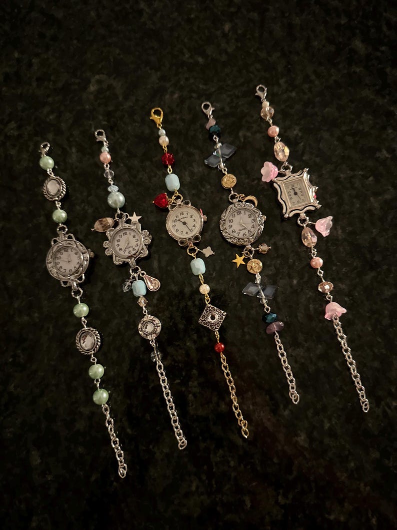 May include: Six charm bracelets with different colored beads and charms, each featuring a small watch face. The watches have silver and gold accents and are surrounded by various charms, including stars, flowers, and crystals.