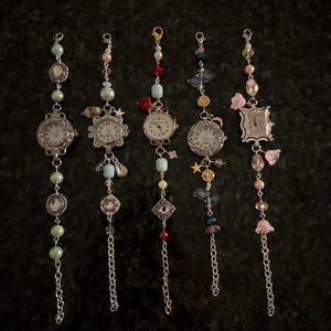May include: Five silver charm bracelets with different colored beads and charms. Each bracelet has a small silver watch face with black hands and Roman numeral markings.