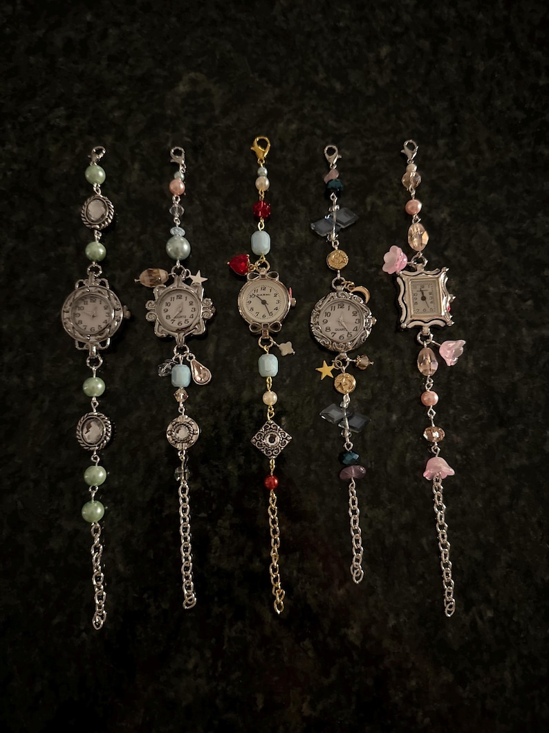 May include: Five silver charm bracelets with different colored beads and charms. Each bracelet has a small silver watch face with black hands and Roman numeral markings.