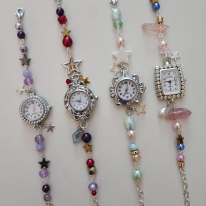 May include: Four decorative watch charms with silver-toned watch faces and beaded chains. Each charm features a different watch face design, with colorful beads, stars, and other embellishments in shades of purple, red, pink, and gold.