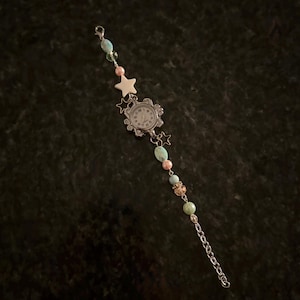 May include: A silver-toned watch with a white face and black numerals, adorned with a beaded bracelet. The bracelet features turquoise, pink, and gold-toned beads, along with star-shaped charms. A delicate chain completes the design.