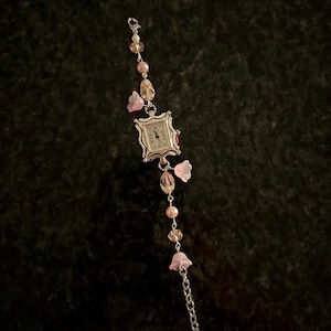 May include: A silver watch with a square face and a beaded chain strap. The beads are pink, white, and clear. The watch has a floral design with pink flowers.
