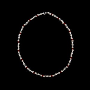 May include: A silver and white beaded necklace with red accents. The necklace is made of small, round beads and has a simple clasp.