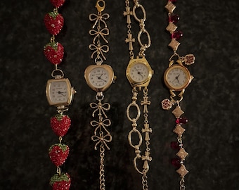 Könnte beinhalten: Vier dekorative Armbanduhren mit goldfarbenen Metallketten. Eine Uhr hat ein Erdbeer-Design, eine andere ein herzförmiges Zifferblatt, und zwei weitere haben runde Zifferblätter. Die Zifferblätter der Uhren haben weiße Hintergründe und schwarze Zahlen.