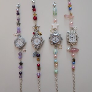 May include: Four decorative watch charms with silver-toned watch faces and beaded chains. Each charm features a different watch face shape and is adorned with colorful beads, stars, and crystals. The charms are designed to be attached to a bag or keychain.