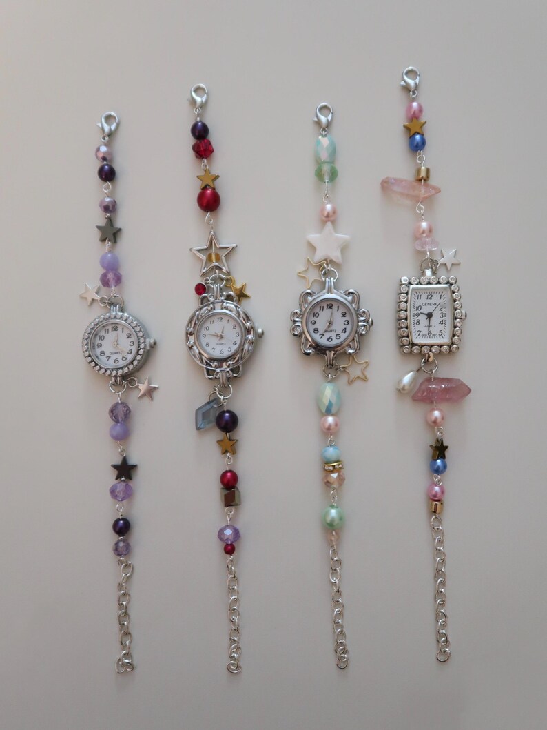 May include: Four decorative watch charms with silver-toned watch faces and beaded chains. Each charm features a different watch face shape and is adorned with colorful beads, stars, and crystals. The charms are designed to be attached to a bag or keychain.