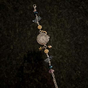 May include: A silver watch with a white face and black Roman numeral markings. The watch is attached to a silver chain with various colored beads, including blue, pink, and gold.