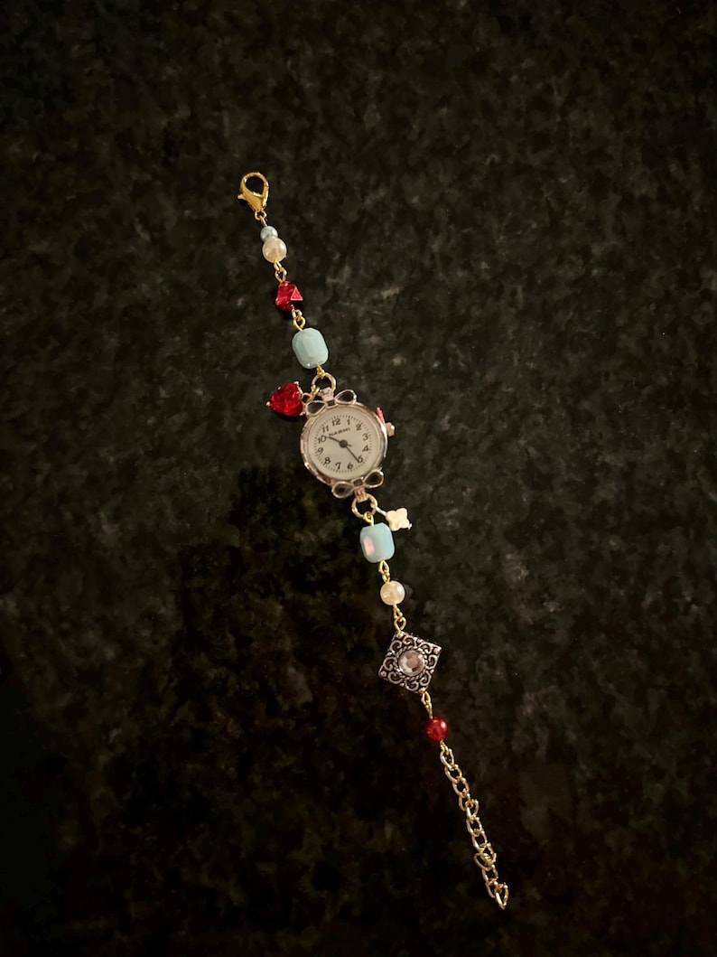 May include: A gold chain bracelet with a small watch face, red and blue beads, and a silver charm with a clear stone.