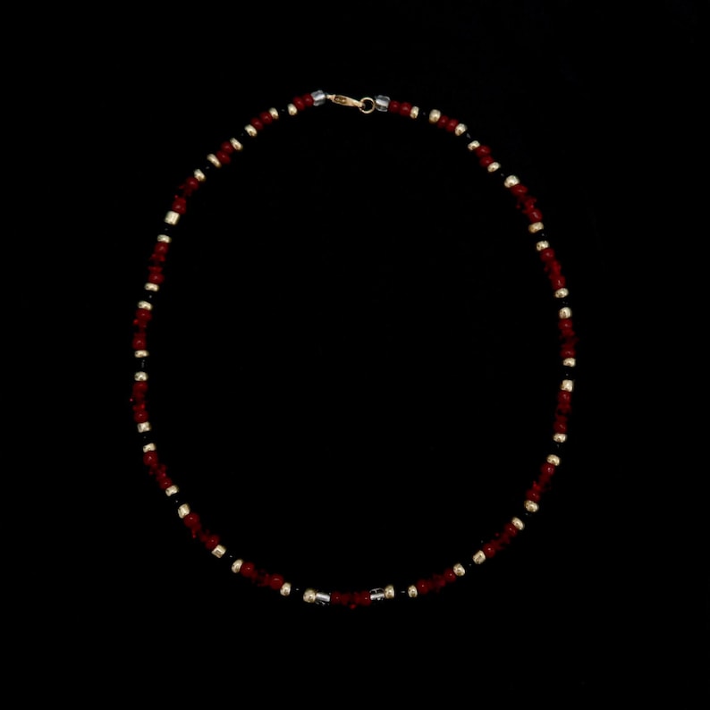May include: A red and black beaded necklace with a gold clasp.