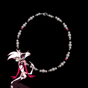 May include: A white pearl necklace with black and pink accents. The necklace is circular and has a silver clasp.