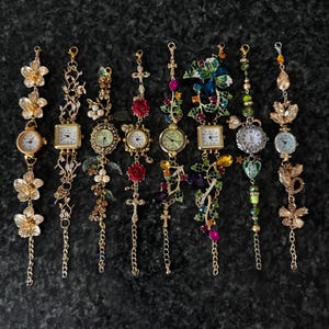 May include: An assortment of ornate, decorative wristwatches with gold-toned metal and various embellishments. Each watch features a different design, including floral, cross, and gemstone accents, with delicate chains and watch faces.