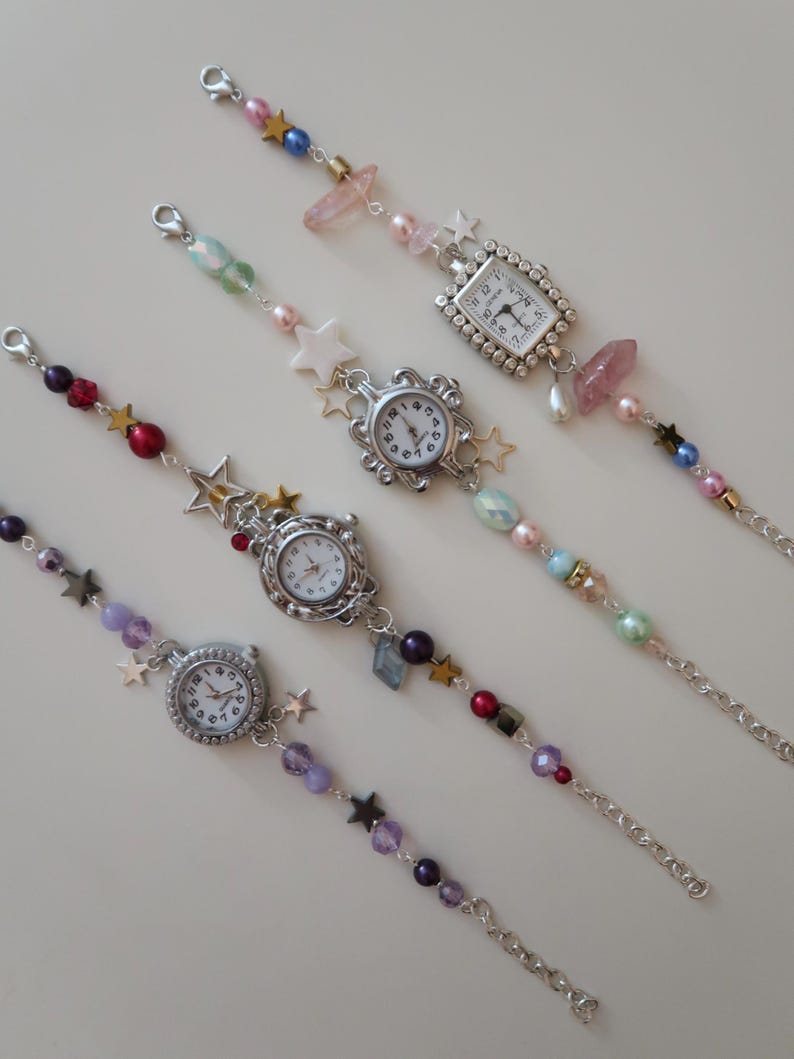 May include: Five beaded charm bracelets with small, round watch faces. The bracelets feature a variety of colorful beads, including pearls, stars, and crystals. The watch faces have silver-colored frames and white dials with black numbers.