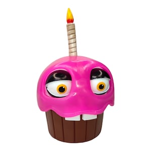 Könnte beinhalten: Eine rosa cupcake-förmige Figur mit großen, ausdrucksstarken Augen und zwei weißen Zähnen. Eine Kerze mit gelber Flamme sitzt auf dem Cupcake. Der Boden des Cupcakes ist braun.