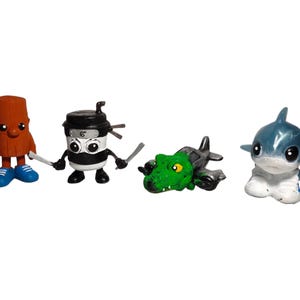 May include: Four small, cartoonish figurines. A brown log with a baseball bat, a black and white ninja coffee cup with swords, a green dinosaur on a plane, and a blue shark with white accents.