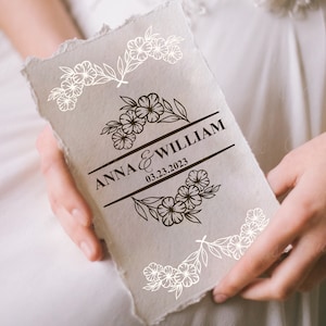 May include: A white card with a brown floral design and the text "ANNA & WILLIAM 03.23.2023" in a black banner.