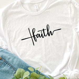 Puede incluir: Camiseta blanca con la palabra "faith" escrita en cursiva negra.