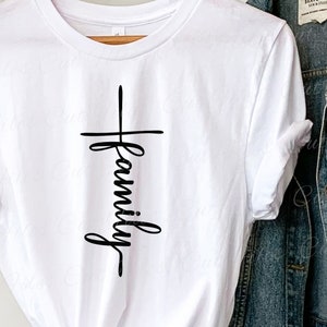 Puede incluir: Camiseta blanca con un gr&aacute;fico negro de una cruz con la palabra "familia" escrita verticalmente en el centro.