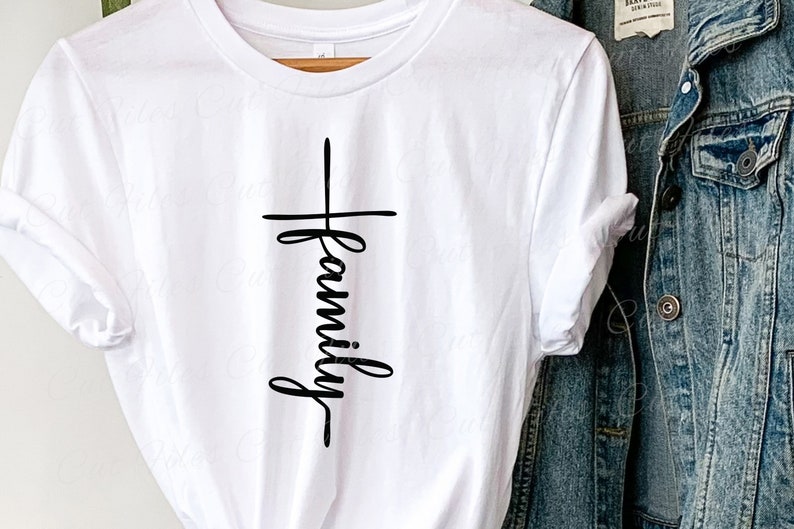 Puede incluir: Camiseta blanca con un gr&aacute;fico negro de una cruz con la palabra "familia" escrita verticalmente en el centro.