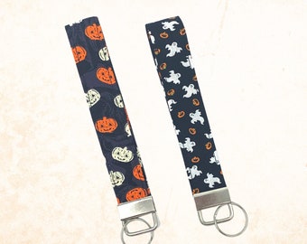 May include: Two black fabric keychains with silver key rings. One keychain has a pattern of orange pumpkins and white ghosts. The other keychain has a pattern of white ghosts and orange pumpkins.