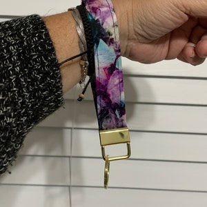 May include: A purple and blue floral patterned key chain with a gold metal ring and clasp.