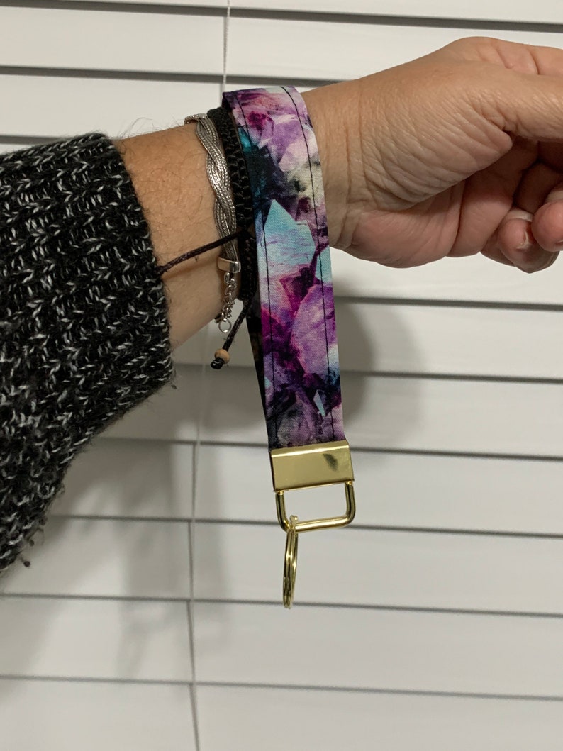 May include: A purple and blue floral patterned key chain with a gold metal ring and clasp.