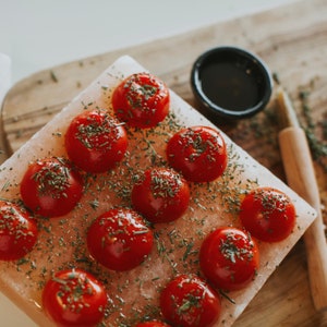 Op de afbeelding: Een roze Himalaya-zoutblok met kleine rode tomaten en groene kruiden erop.
