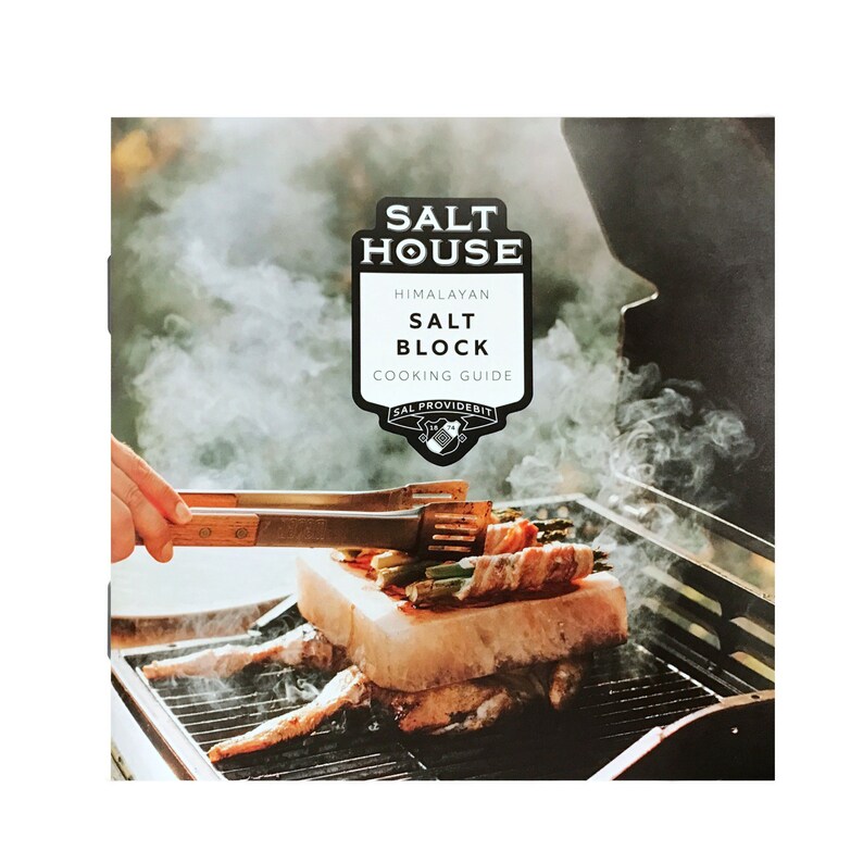 Op de afbeelding: Een kookgids voor Himalaya-zoutblokken met een close-up afbeelding van een zoutblok op een grill met asperges en spek eromheen gewikkeld. De tekst op de gids luidt "Salt House Himalayan Salt Block Cooking Guide".