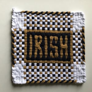 May include: A woven wall hanging with a black and white checkered pattern and a gold border. The word "RICH" is woven in gold letters inside a black rectangle.