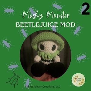 May include: A green and white crocheted mushroom character with black pants and a green and white striped shirt. The character is holding a sign that says "Mushy Monster Beetlejuice Mod 2".